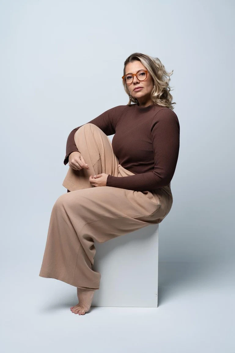 Retrato de Aline Vasconcelos sentada, de óculos e blusa marrom